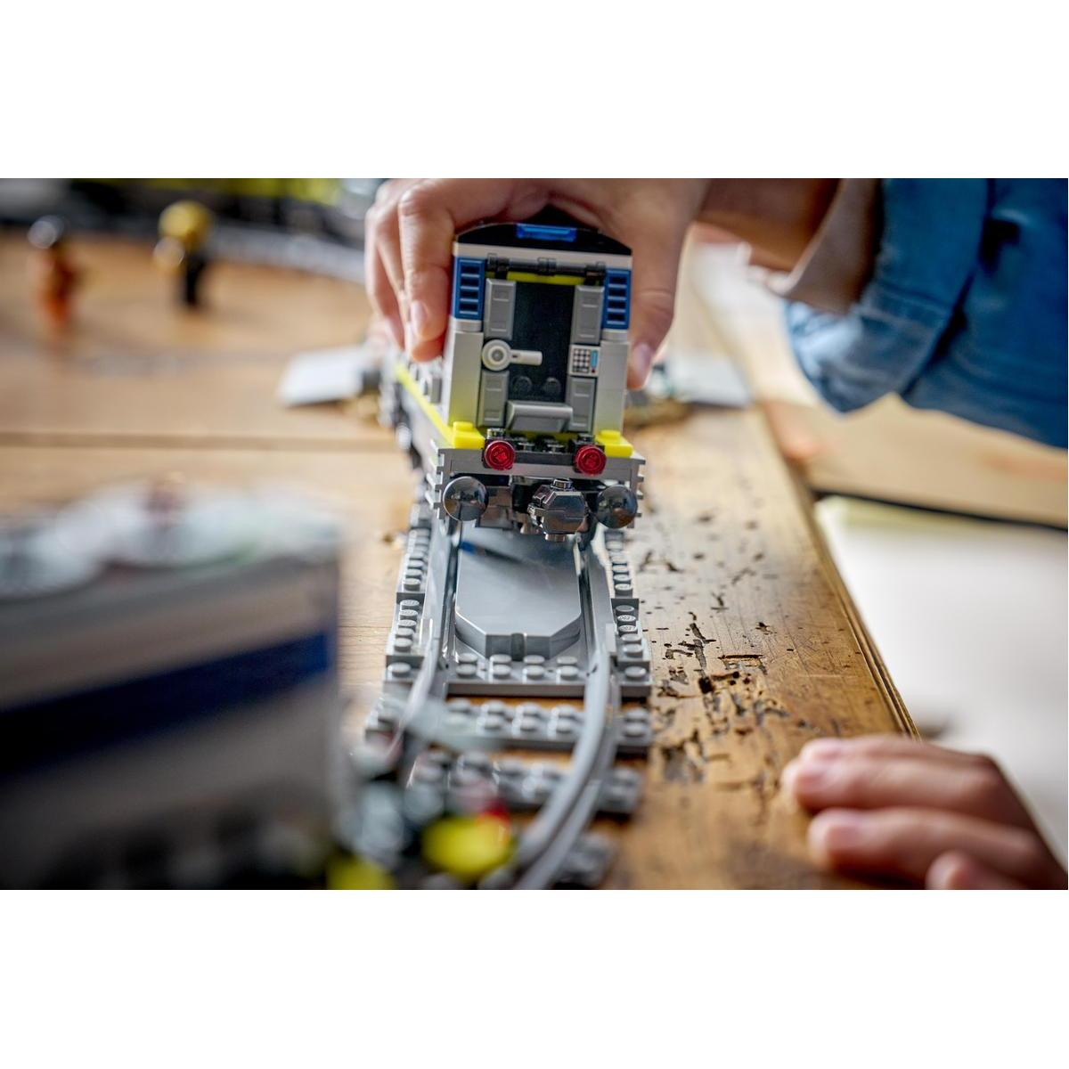 Niño jugando con tren Lego en mesa de madera. Tren amarillo y gris en vías.