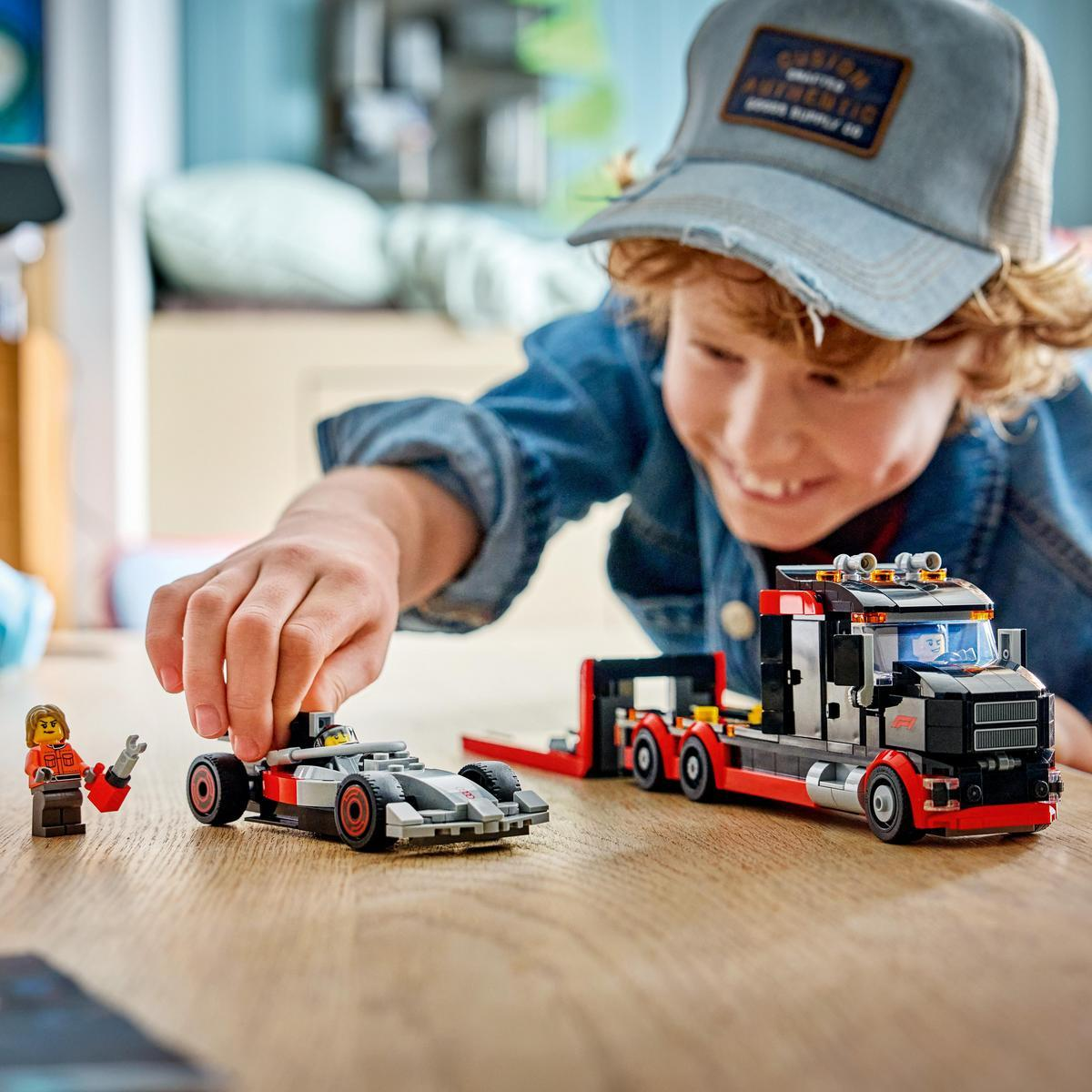 Un niño juega con coche de carreras y camión LEGO. El niño lleva chaqueta azul y gorra.
