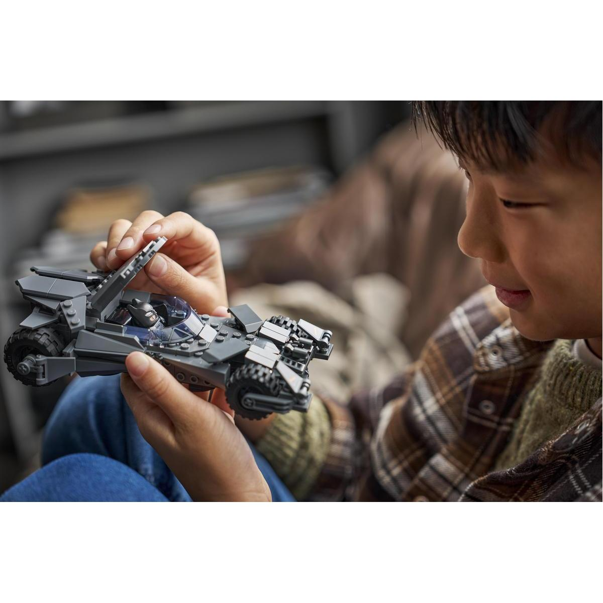 Un bambino tiene in mano un giocattolo Batmobile Lego grigio.