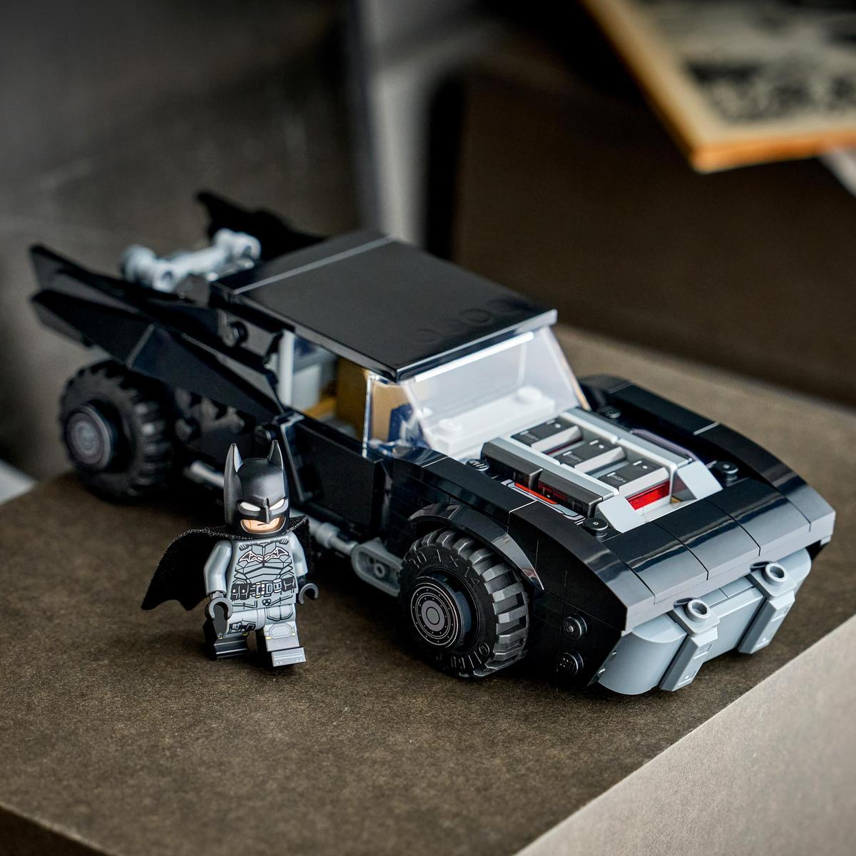 Figurka Lego Batmana stoi obok czarnego Lego Batmobilu na brązowej powierzchni.