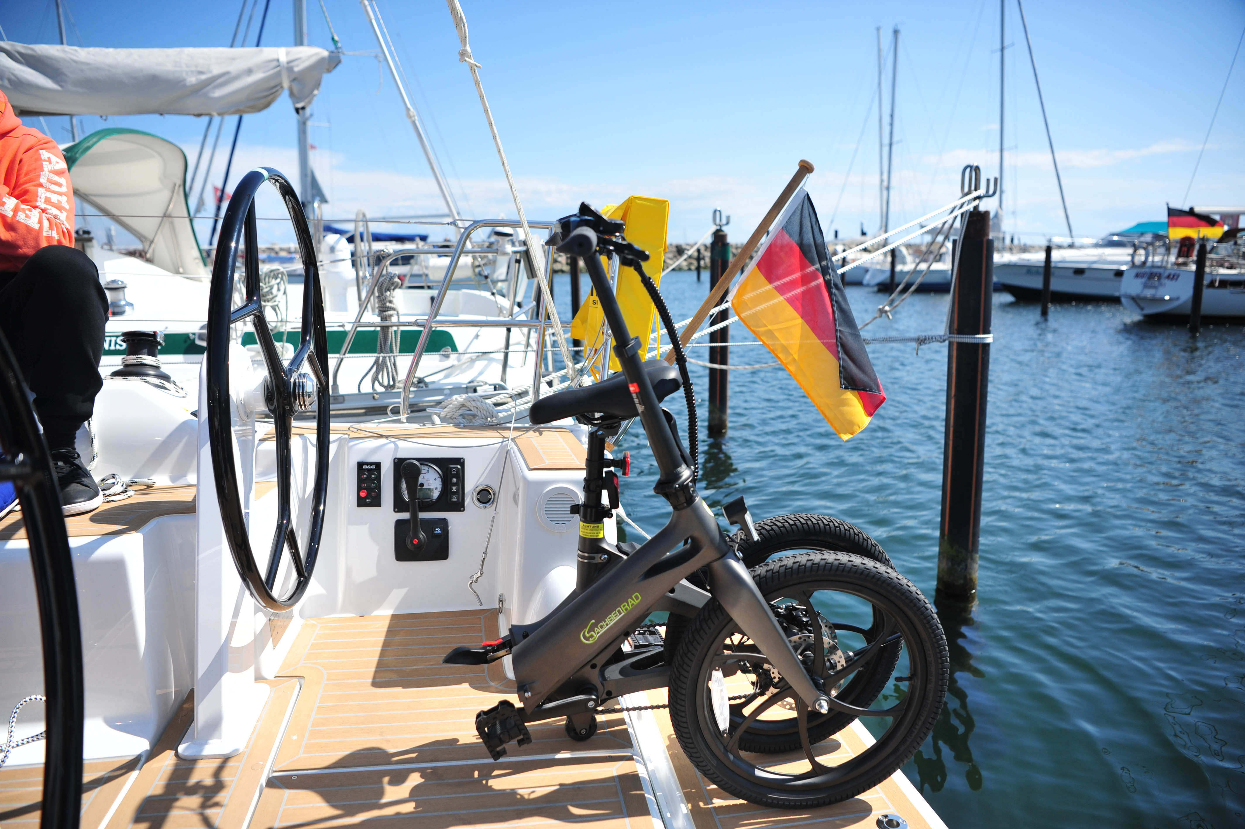 Ein graues Fahrrad steht auf einem Boot neben einem Steuerrad und einer deutschen Flagge.