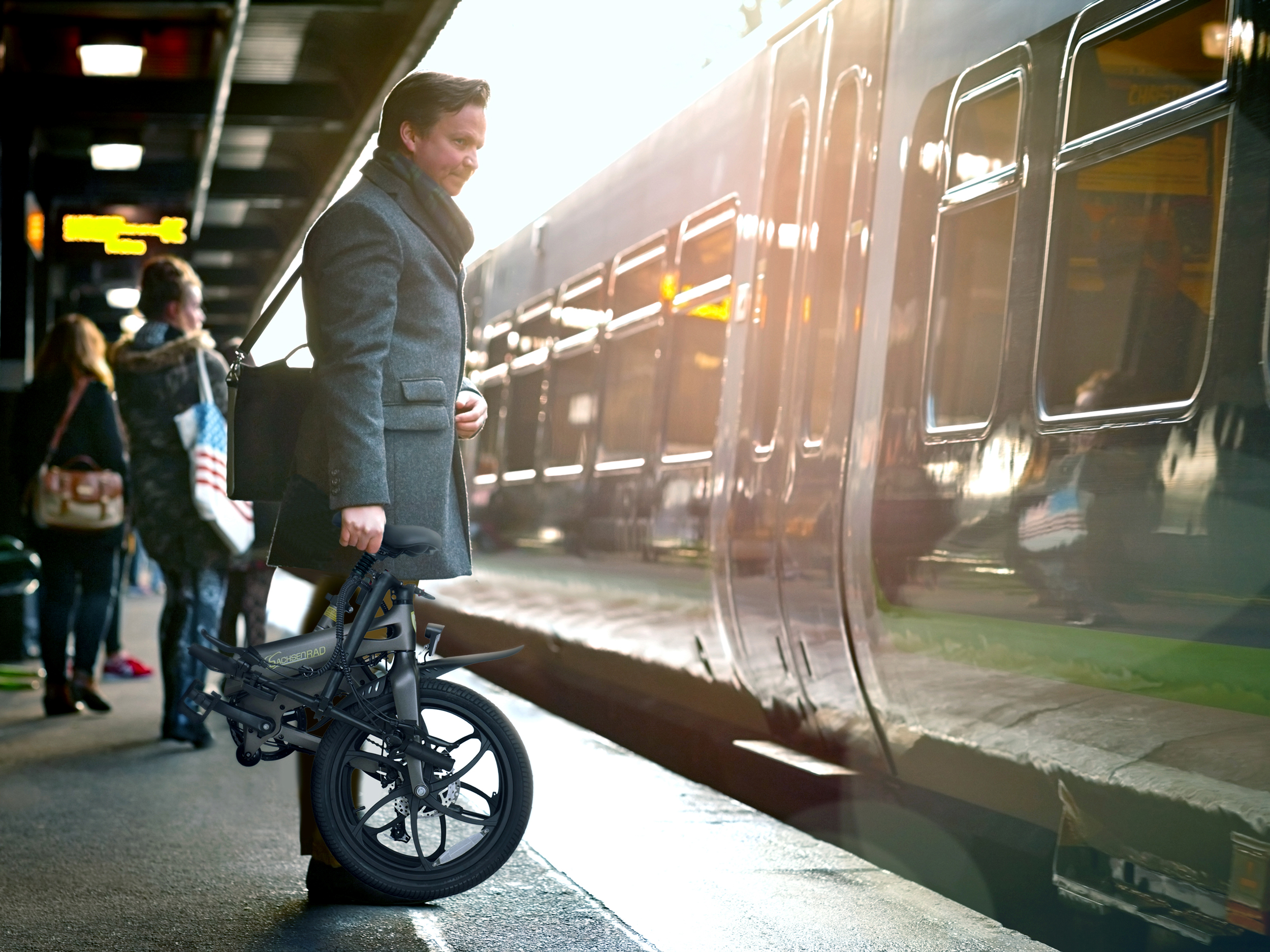 Mann mit faltbarem Fahrrad steht am Bahnsteig neben einem Zug.