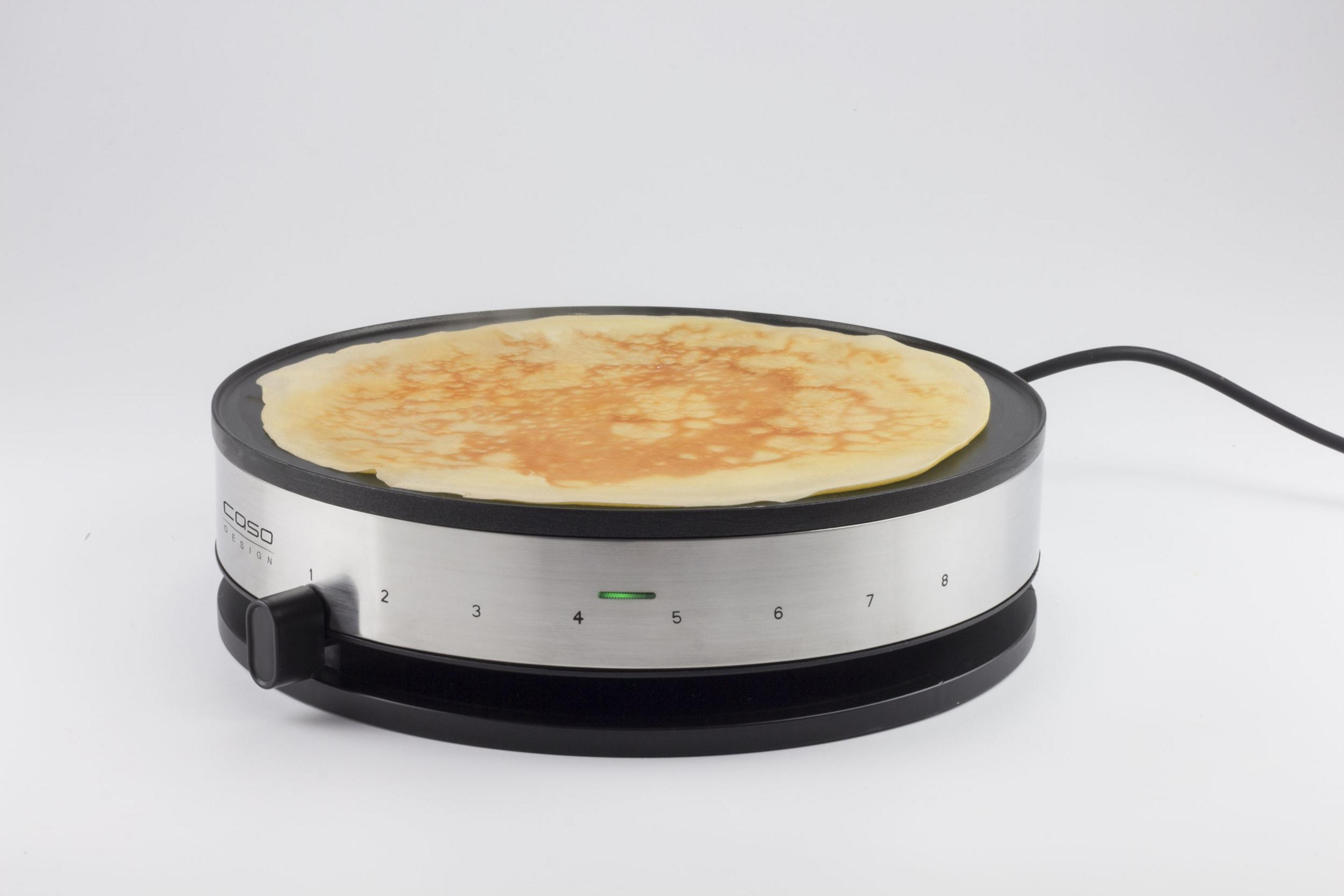 Een pannenkoek bakt op een ronde elektrische bakplaat met genummerde instellingen.