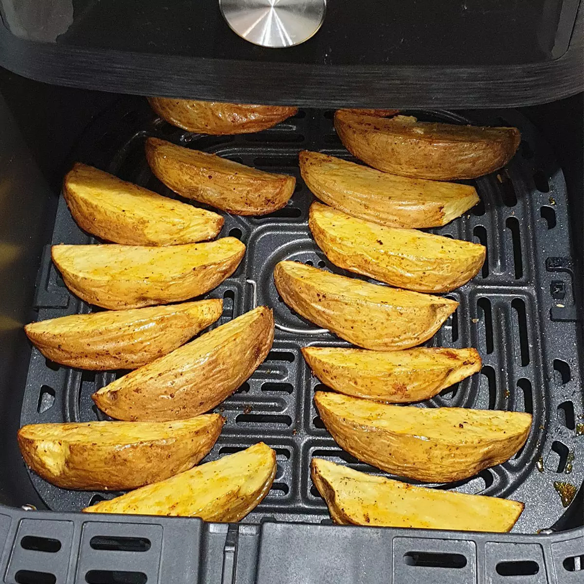 Złocistobrązowe kawałki ziemniaków ułożone w czarnym koszu frytkownicy beztłuszczowej.