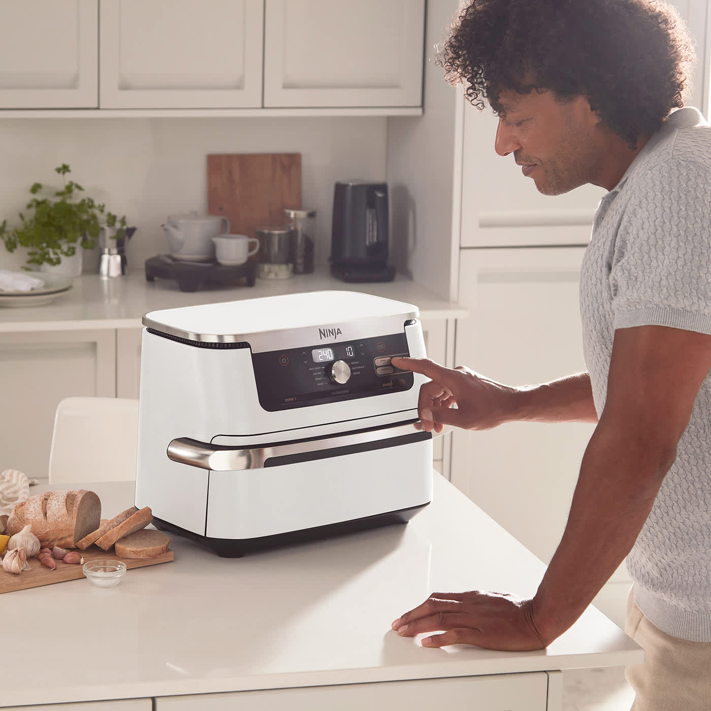 Mężczyzna w kuchni naciska przycisk na białej frytkownicy beztłuszczowej Ninja. Chleb na desce.