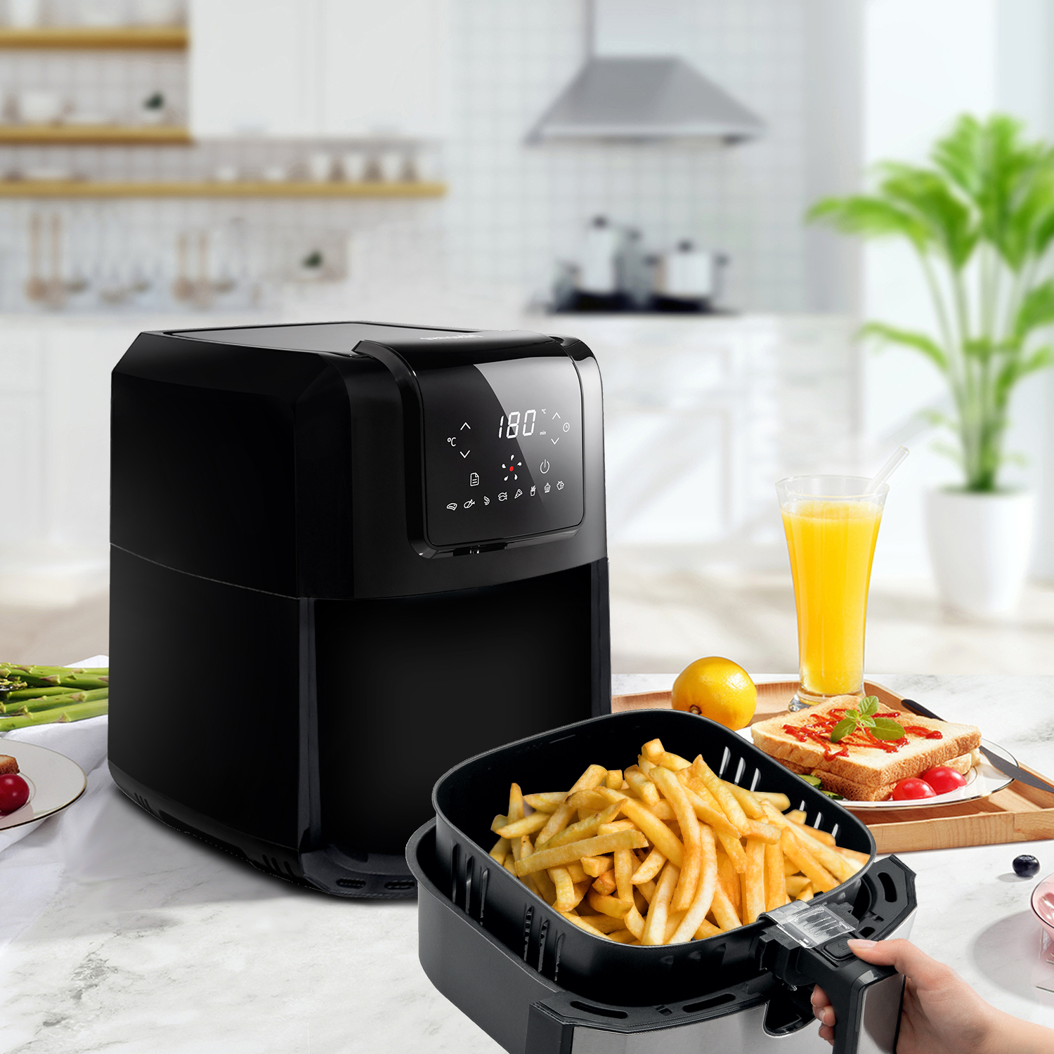 Black air fryer with french fries and orange juice in a kitchen setting.