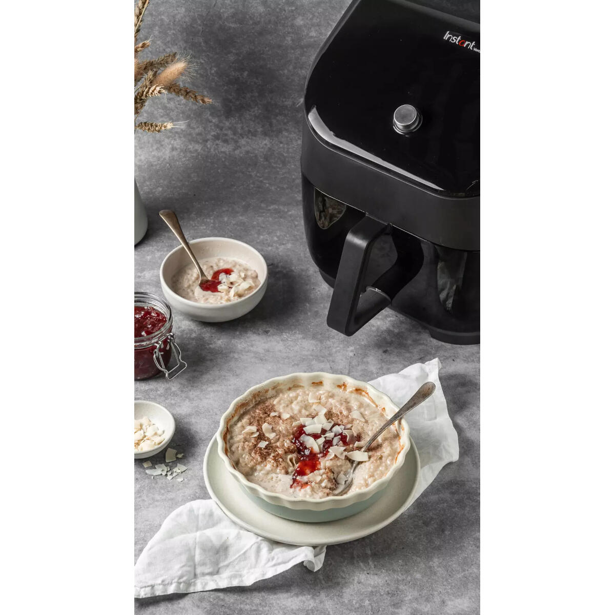 Czarna frytkownica powietrzna obok miseczek owsianki z dżemem i wiórkami kokosowymi.