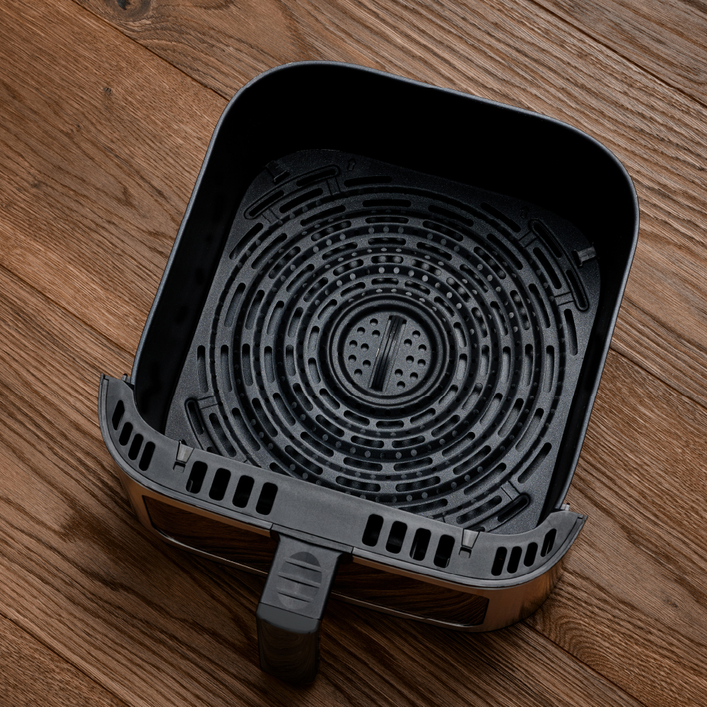 Ein leerer, schwarzer Airfryer-Korb mit Griff auf Holzhintergrund.