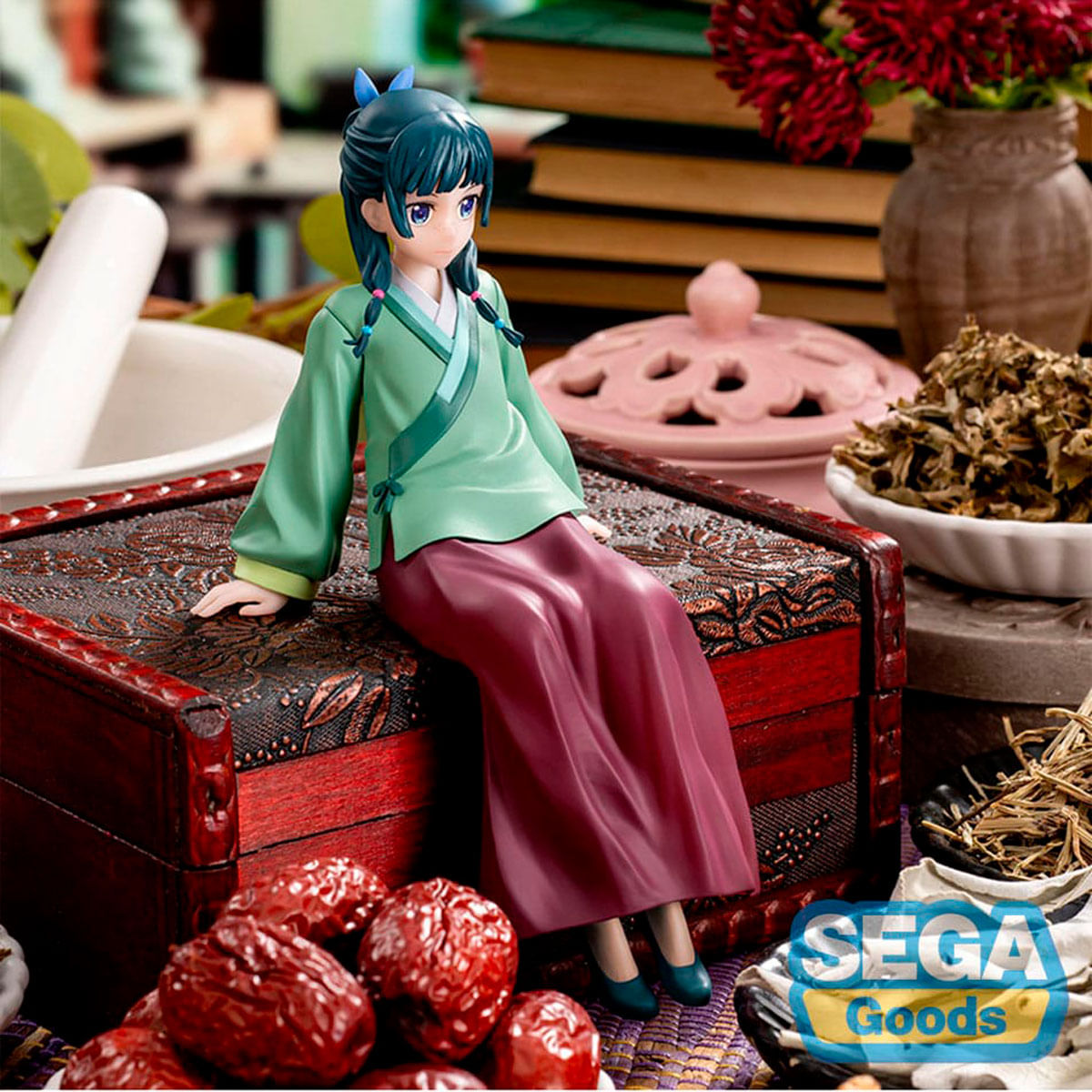 Une figurine de fille en kimono vert est assise sur un coffre orné.