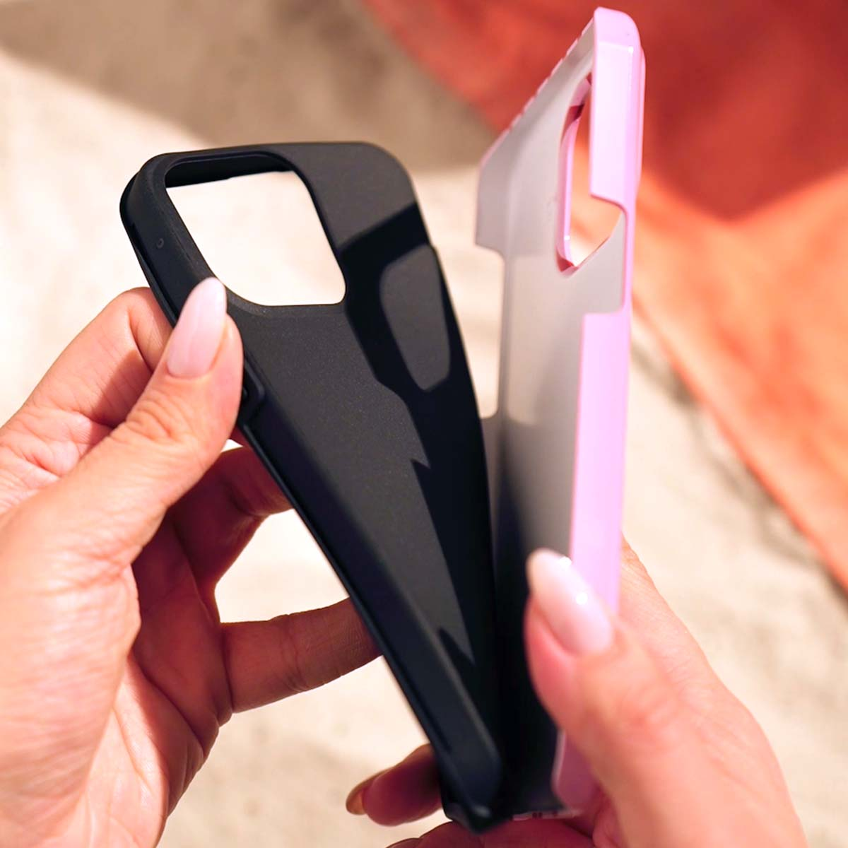 Handen houden een zwart en een roze telefoonhoesje vast.