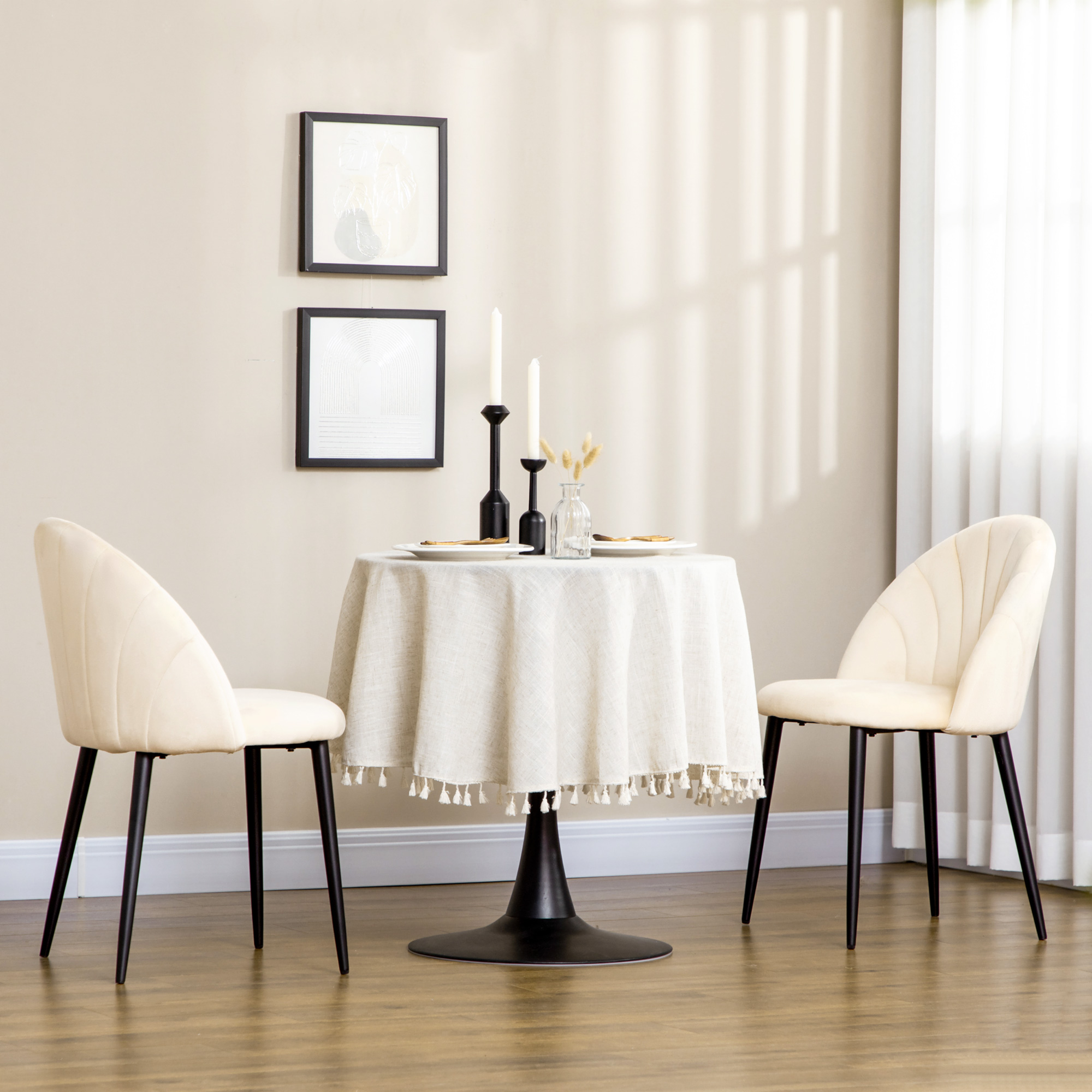 Un tavolo rotondo con tovaglia beige, due sedie e arte da parete.