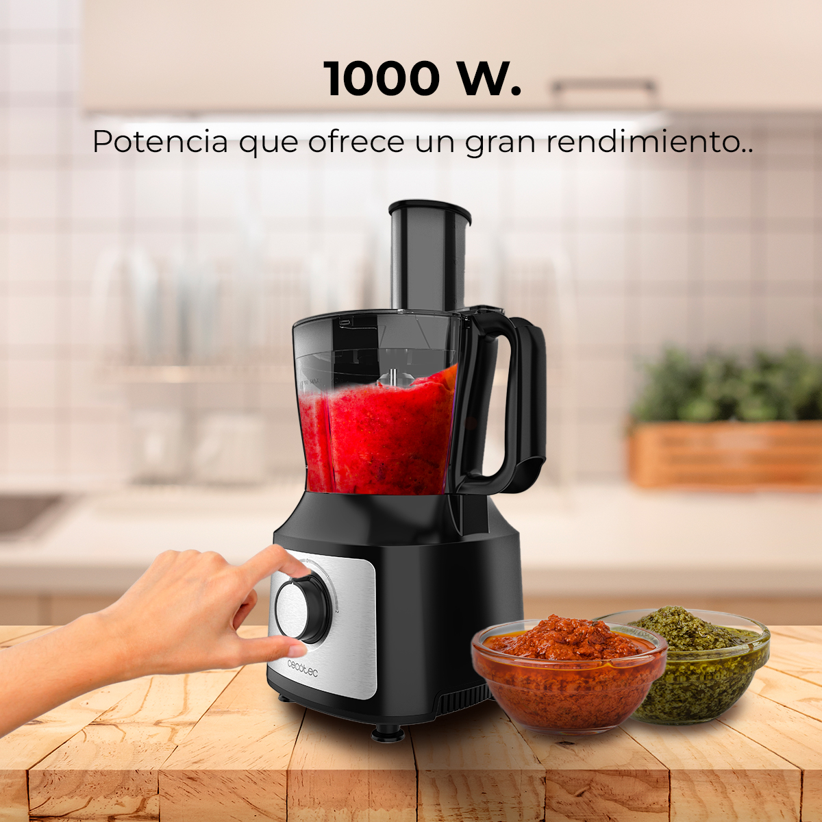 Un procesador de alimentos negro con contenido rojo y dos cuencos de salsas al lado.