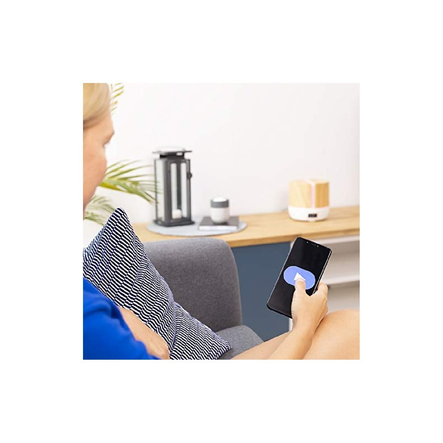 Kobieta siedzi na kanapie, trzyma telefon z przyciskiem play. Poduszka na kolanach.