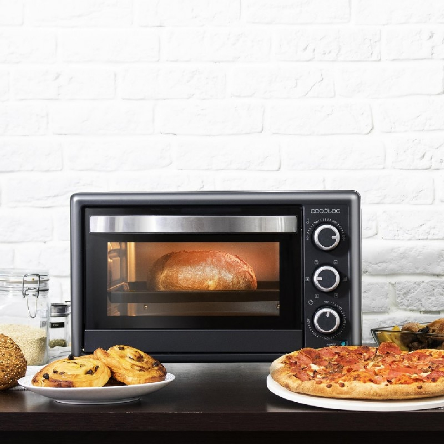 Un piccolo forno con pane, pizza e pasticcini accanto, sfondo di muro di mattoni bianchi.