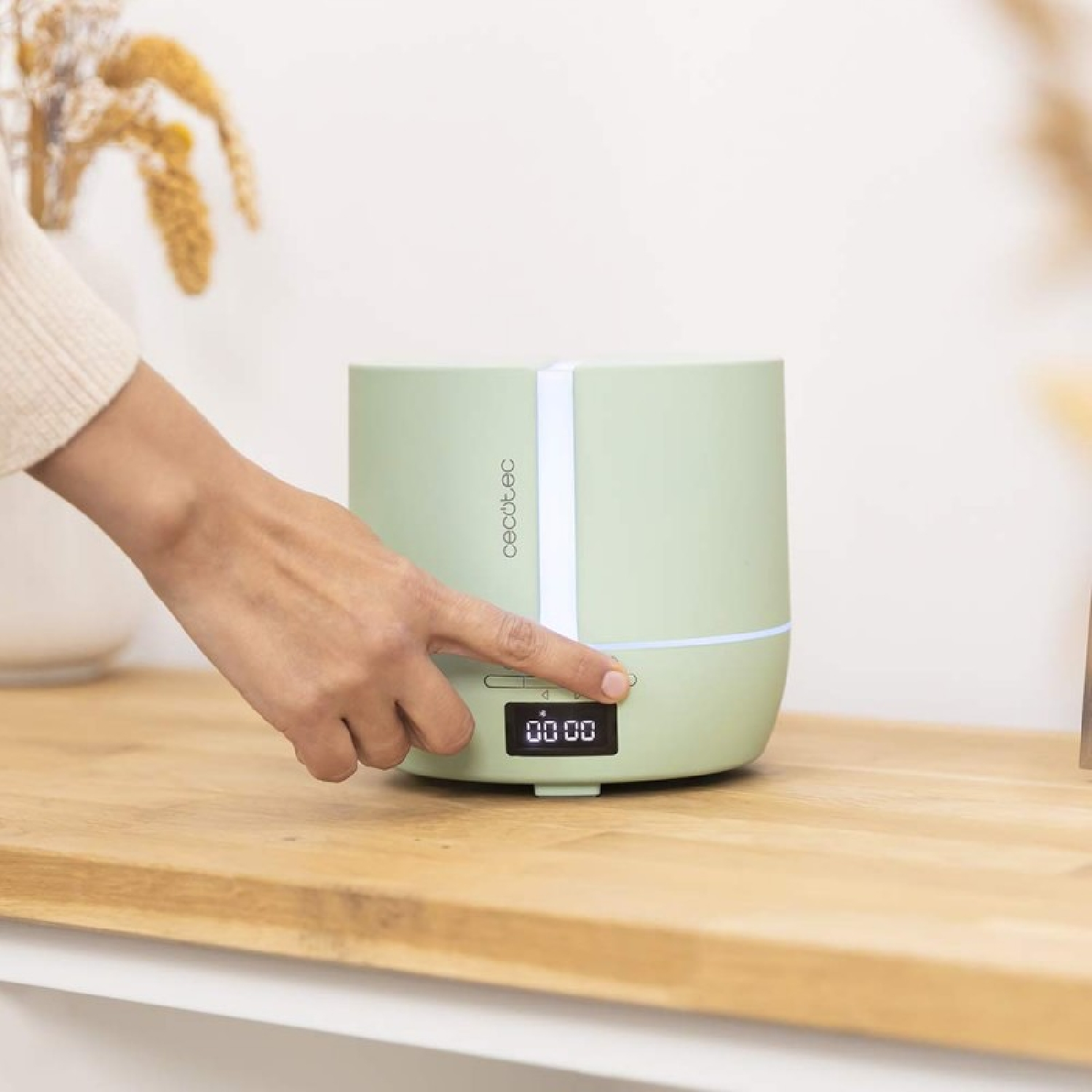 Eine Hand drückt einen Knopf an einem hellgrünen Diffusor mit Digitalanzeige.