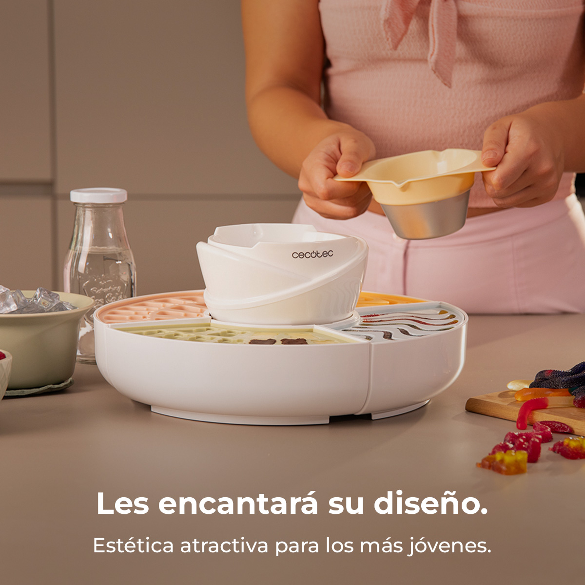 Una persona sujeta un recipiente sobre un aparato. Se ven cubitos de hielo y caramelos.
