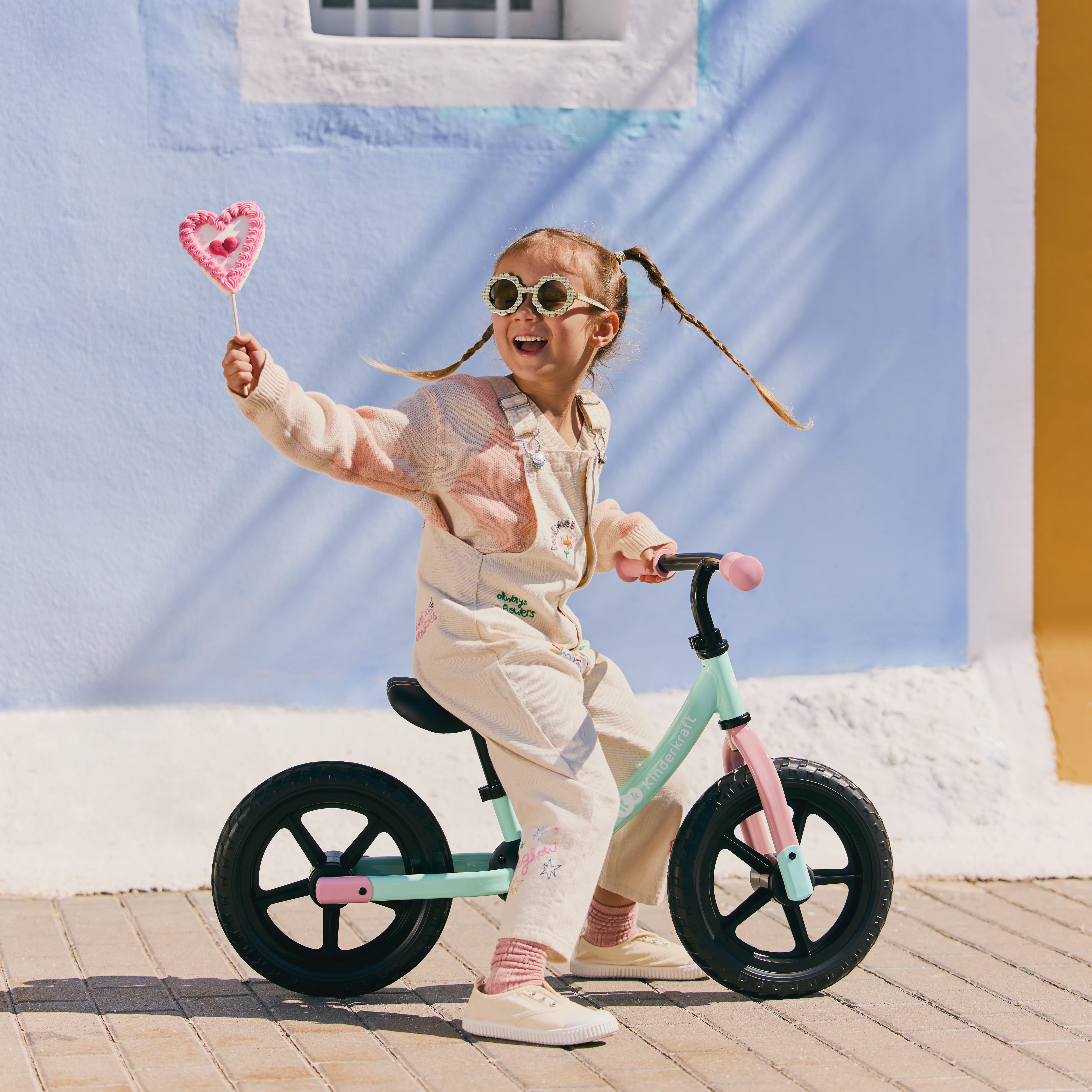 Ein lächelndes Mädchen mit Sonnenbrille fährt ein mintgrünes Fahrrad und hält ein Herz-Lutscher.