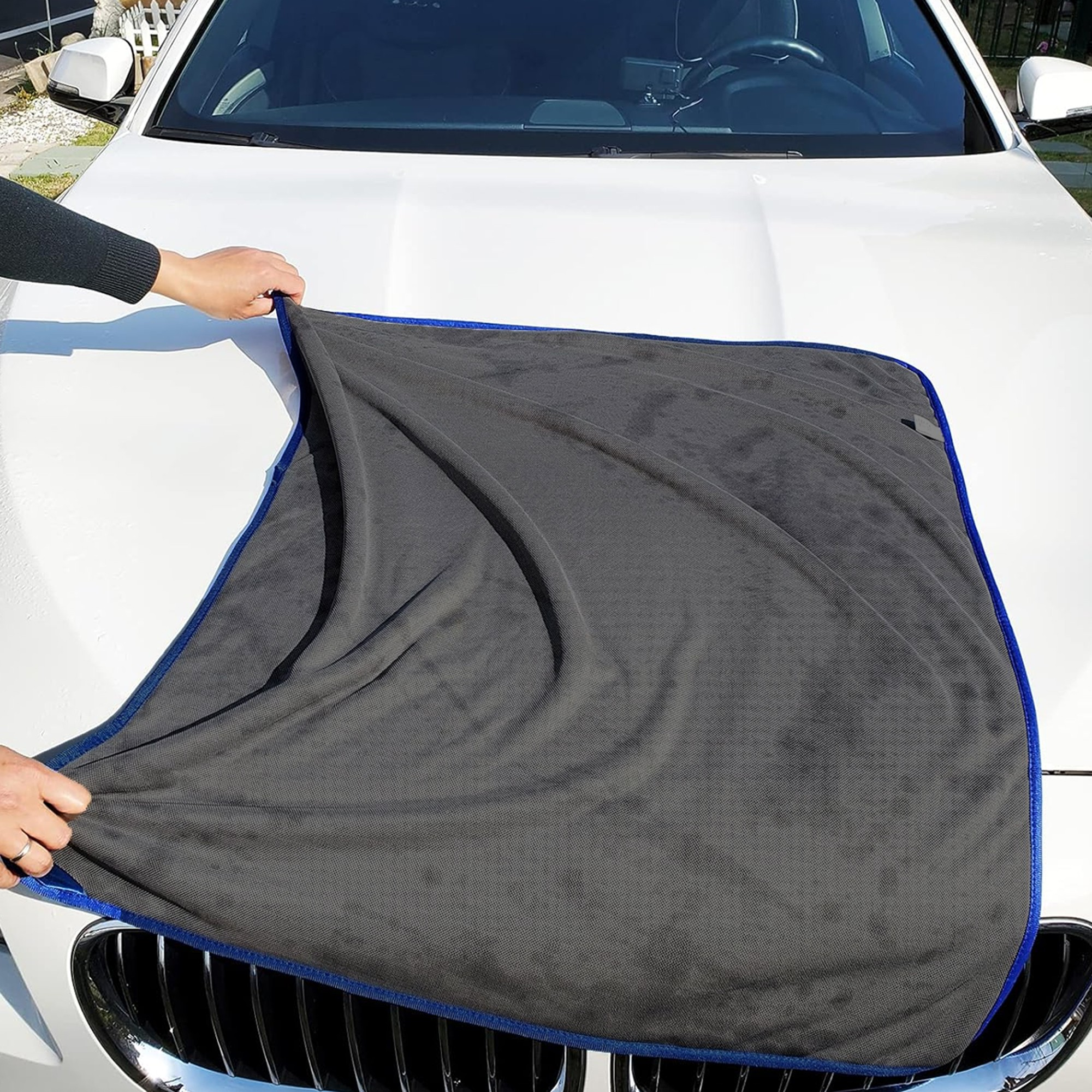 Mavi kenarlı gri mikrofiber bez, beyaz araba kaputuna seriliyor.