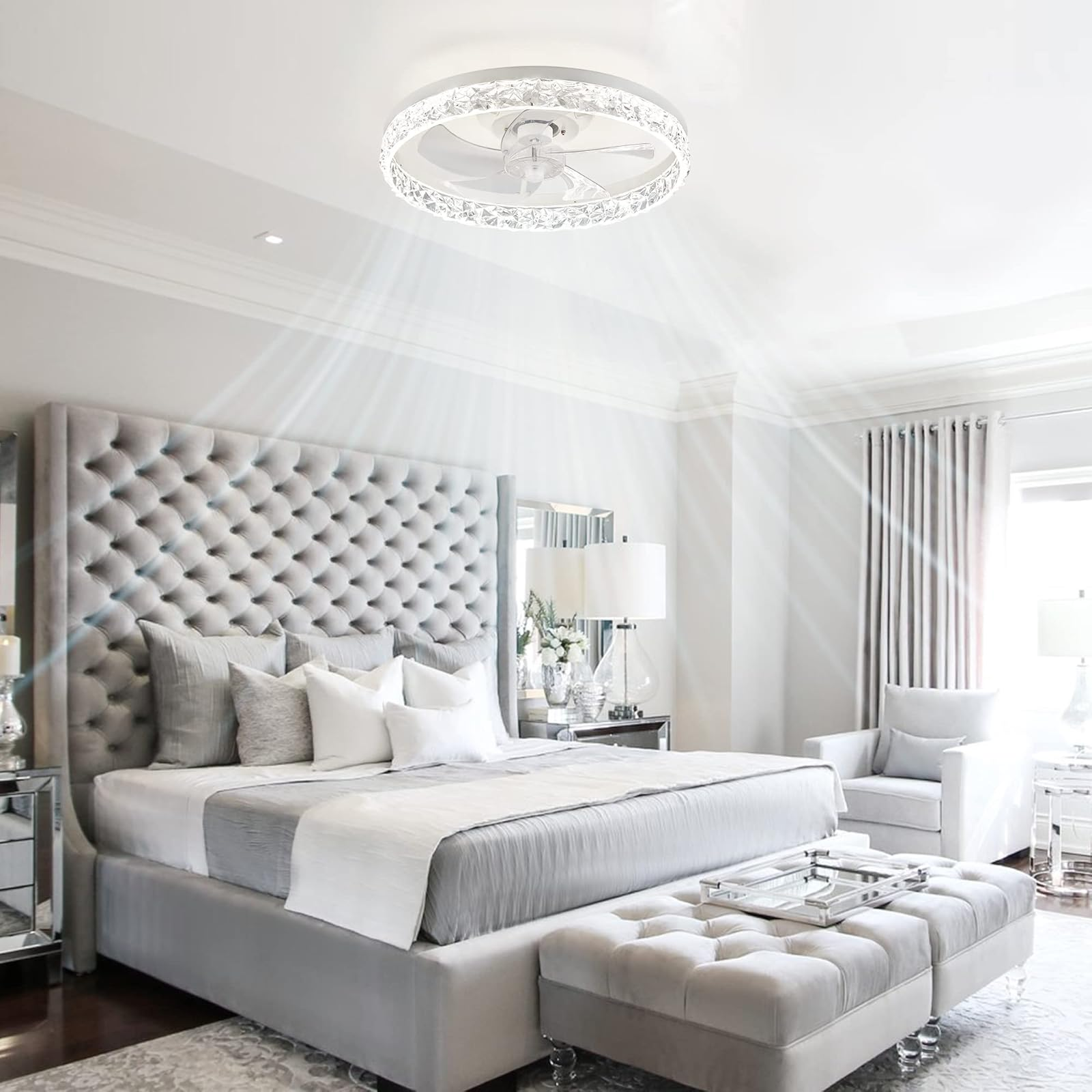 Dormitorio de lujo con cama gris tapizada, lámpara de araña de cristal y luz natural.