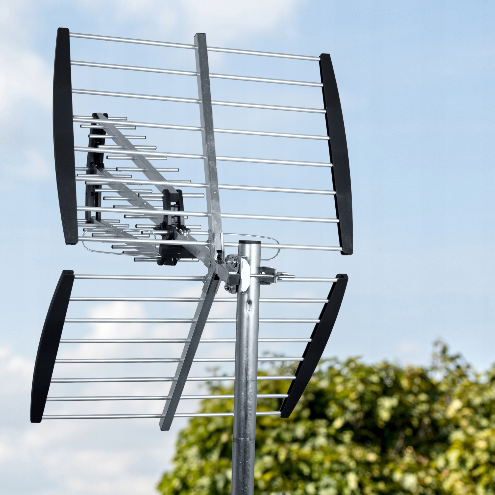 Antena telewizyjna z czarnymi elementami na słupie na tle niebieskiego nieba.