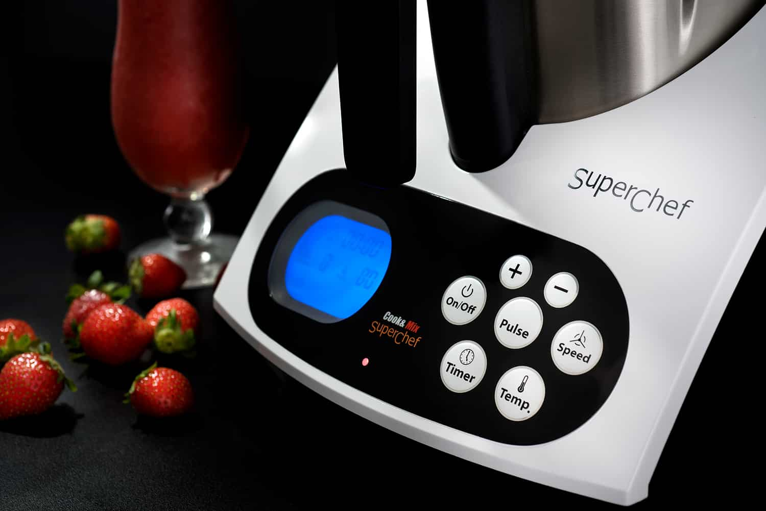 Un electrodoméstico de cocina con un vaso de bebida de fresa y fresas frescas al lado.