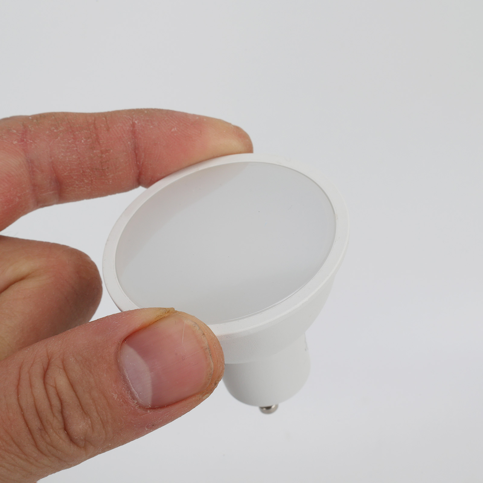 Una mano sostiene una bombilla LED blanca con base GU10.