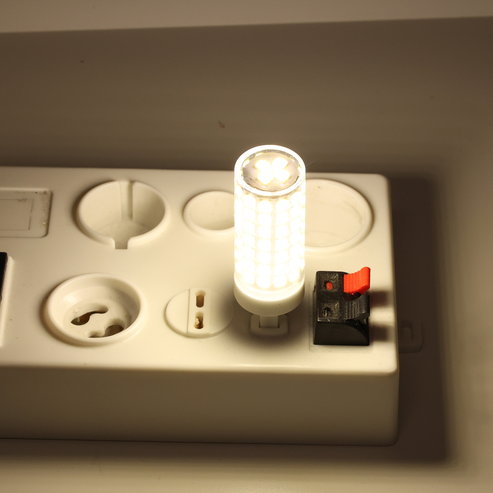 Una bombilla LED encendida se asienta en una regleta blanca con un pequeño interruptor rojo.
