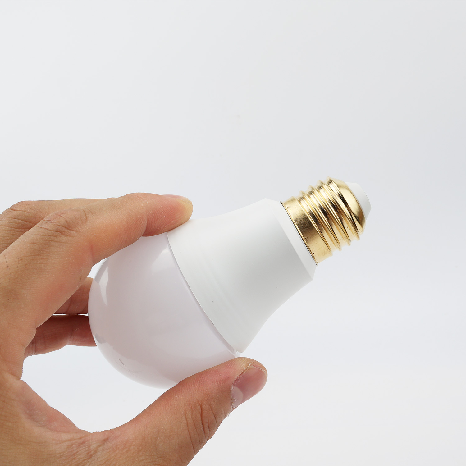 Una mano sostiene una bombilla blanca con base dorada.