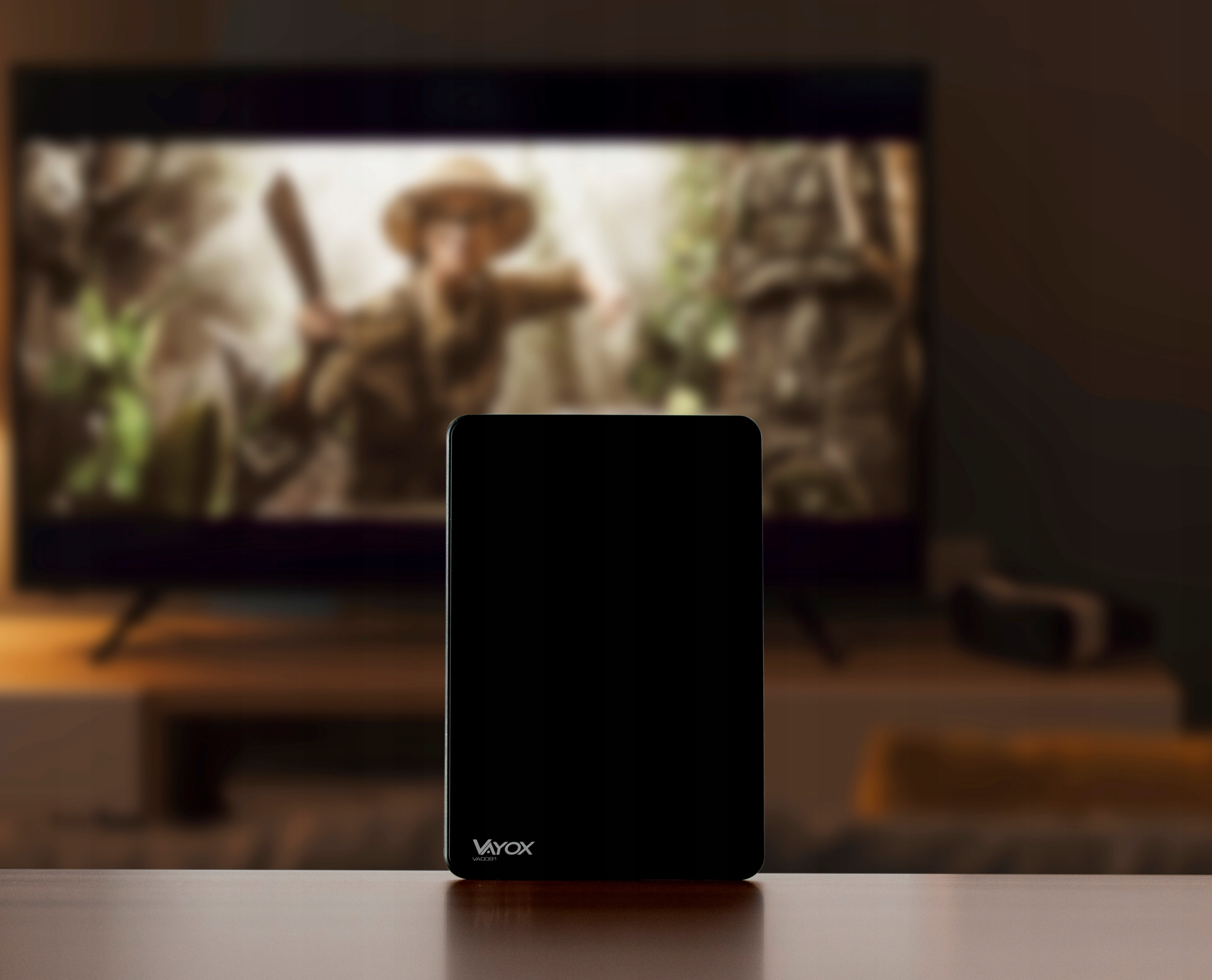 Czarny tablet przed rozmytym telewizorem pokazującym poszukiwacza przygód.