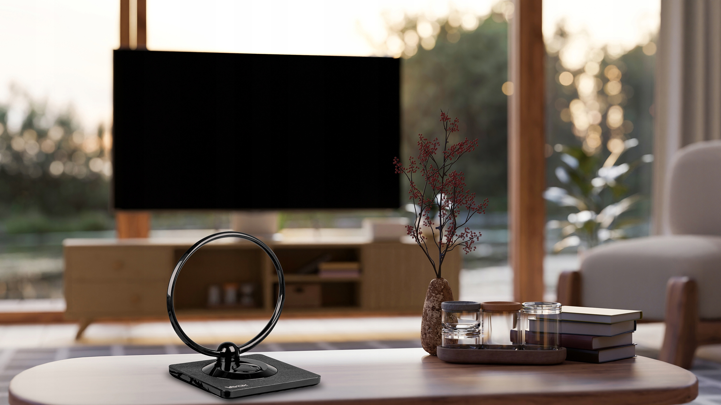 Czarny stojak anteny telewizyjnej stoi na drewnianym stole z książkami i wazonem w tle.