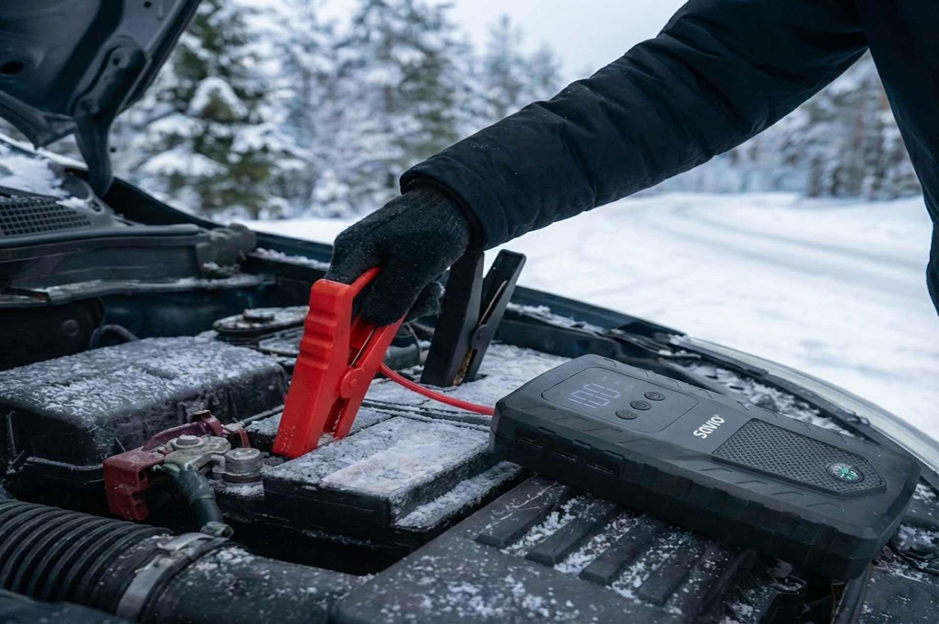 Osoba podłącza kable rozruchowe do akumulatora samochodu na śniegu.