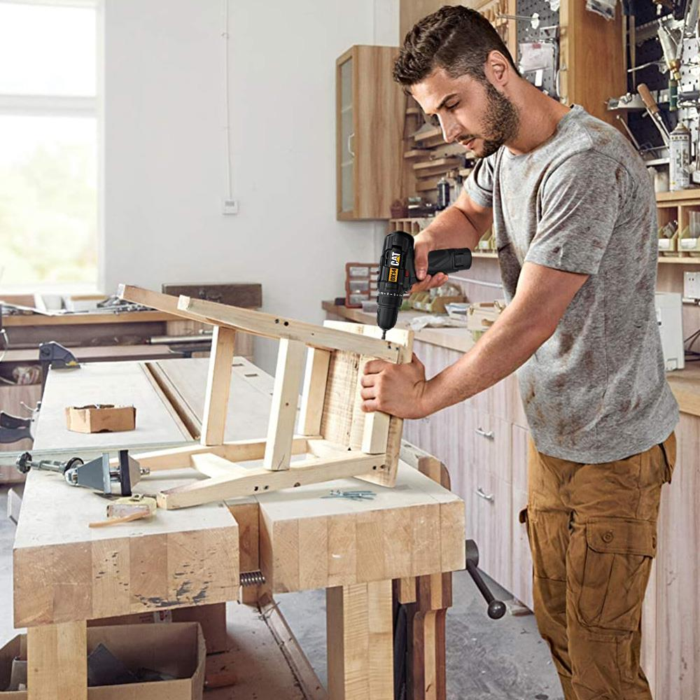 Uomo con barba in officina usa trapano CAT nero su telaio sedia legno.