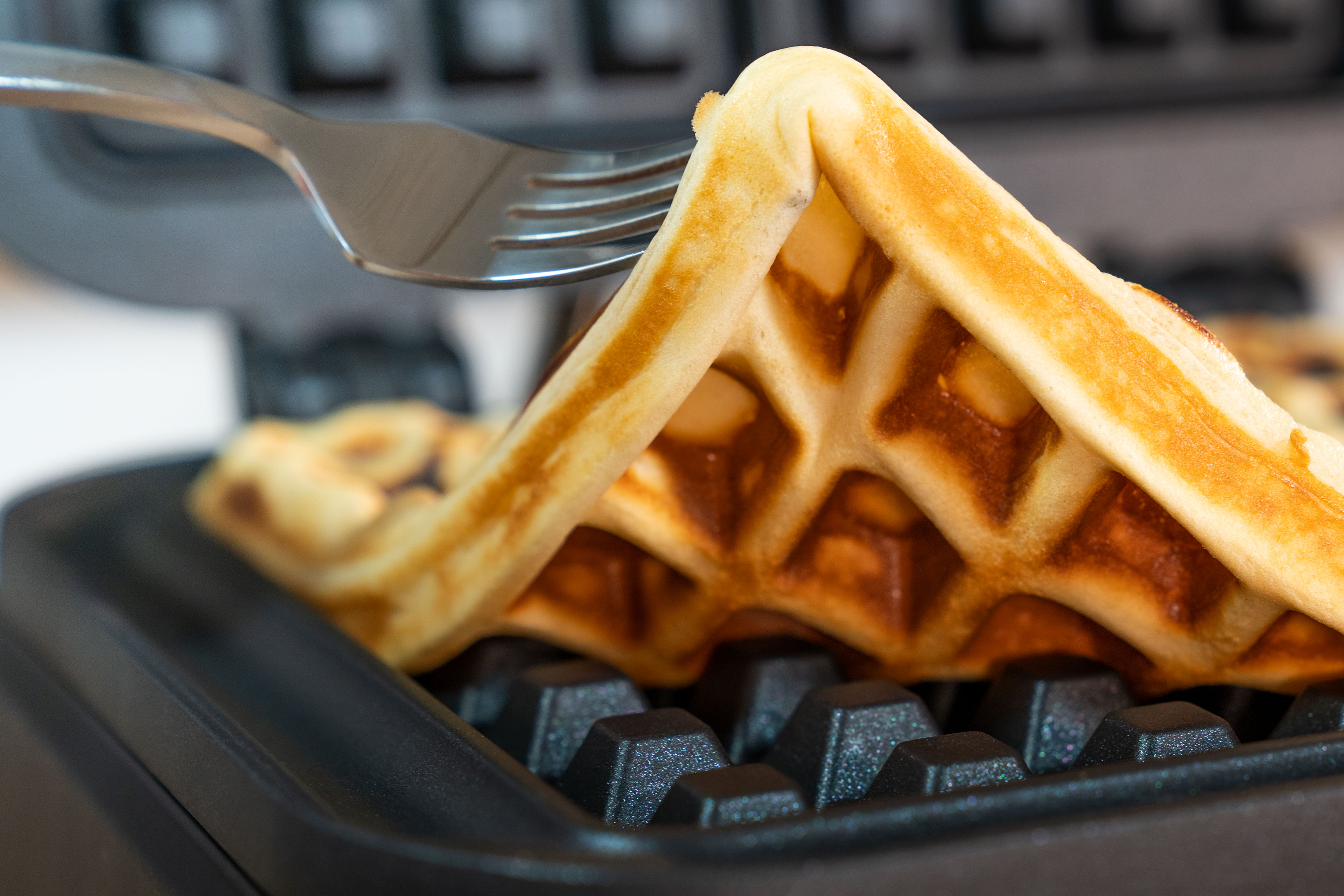 Eine Gabel hebt einen goldenen Waffel aus einem Waffeleisen.