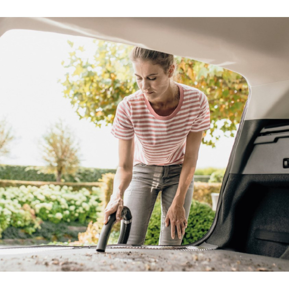 Kobieta odkurza bagażnik samochodu, na zewnątrz z drzewami.