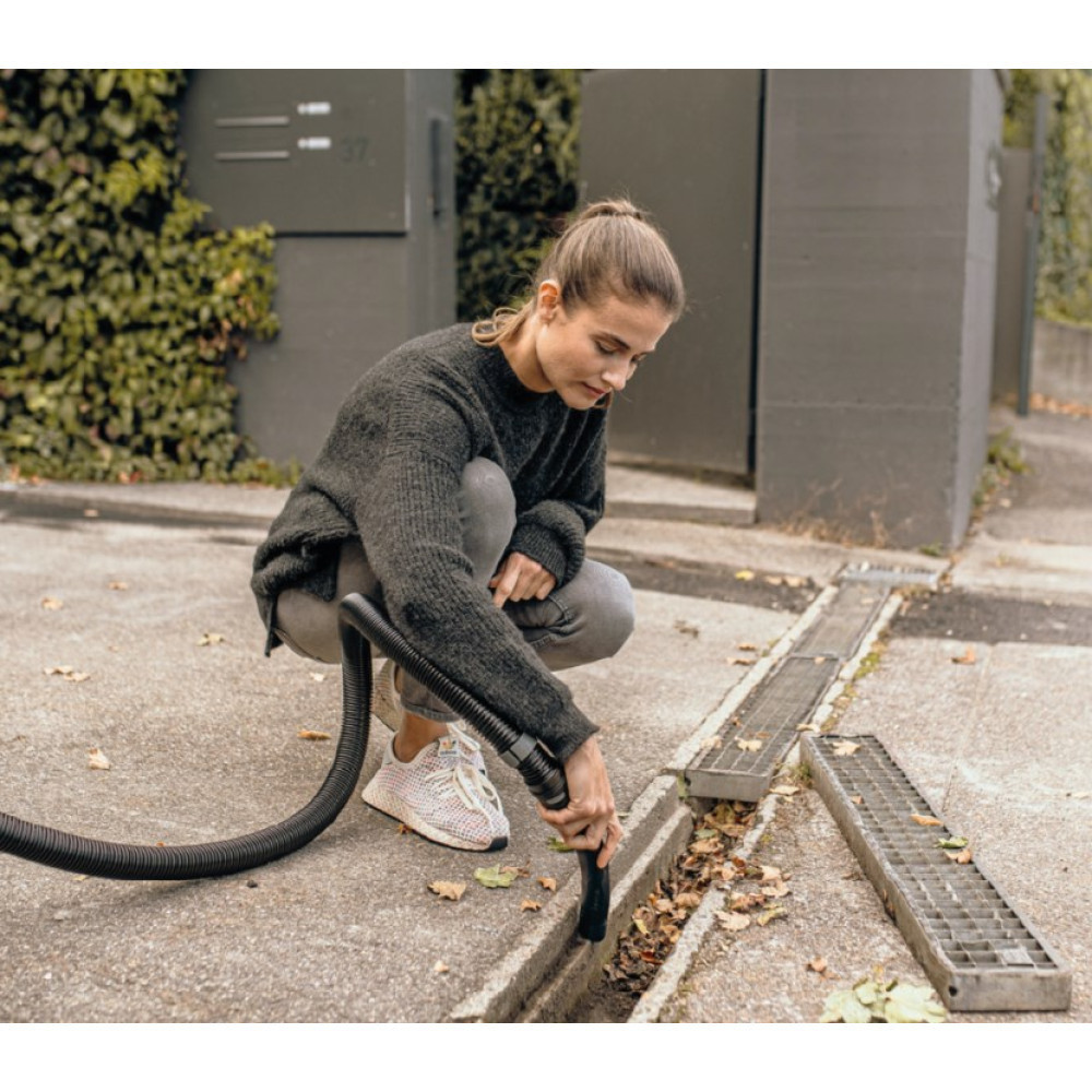 Kobieta odkurza liście z rynny wężem.