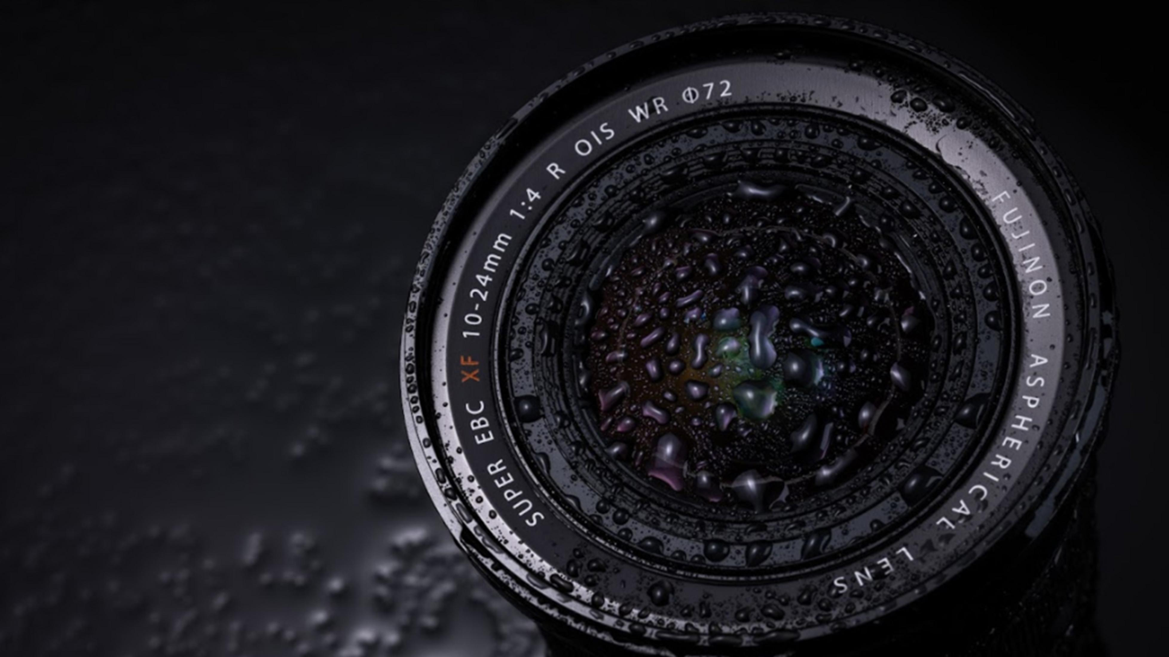 Obiektyw aparatu fotograficznego pokryty kroplami wody na ciemnym tle.