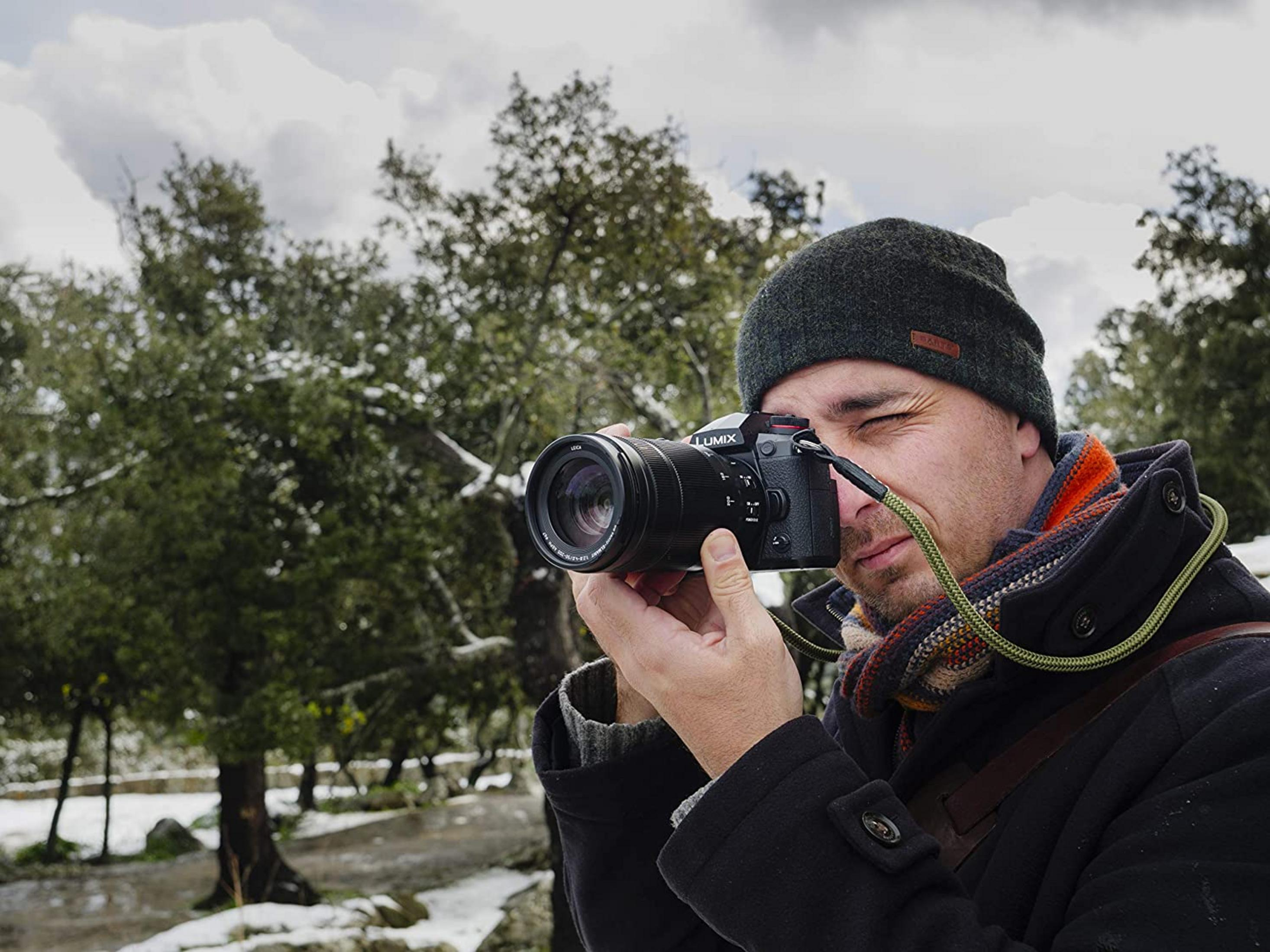 Mann mit Kamera im Freien, verschneite Bäume im Hintergrund.