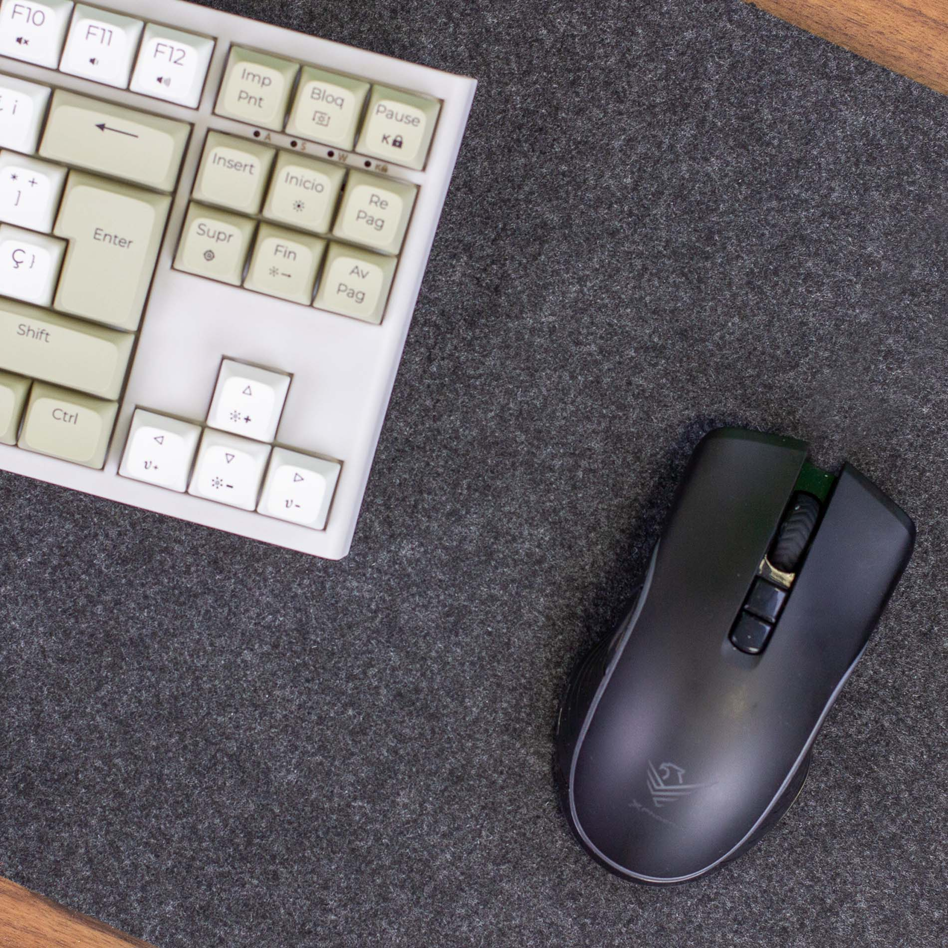 Un teclado de computadora gris y un ratón negro descansan sobre una alfombrilla de fieltro oscura.