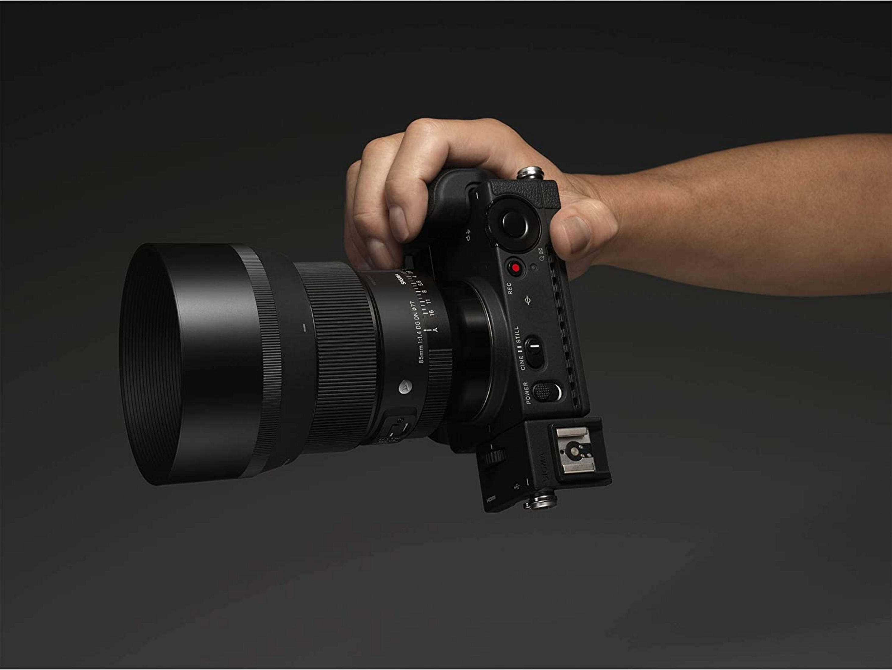 Una mano tiene una fotocamera Sigma nera con un obiettivo grande.