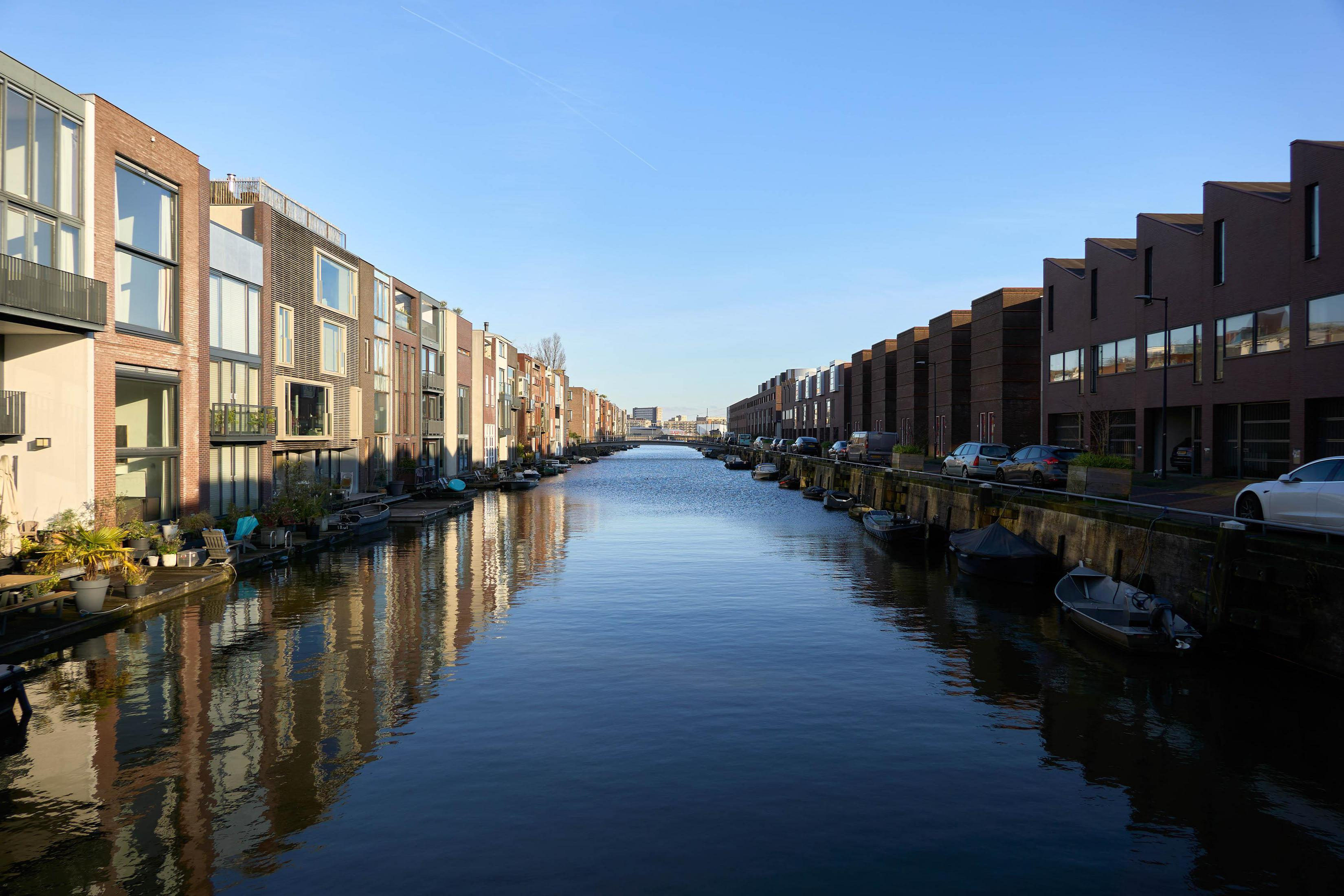 Moderne Häuser säumen einen Kanal mit Spiegelungen im Wasser.