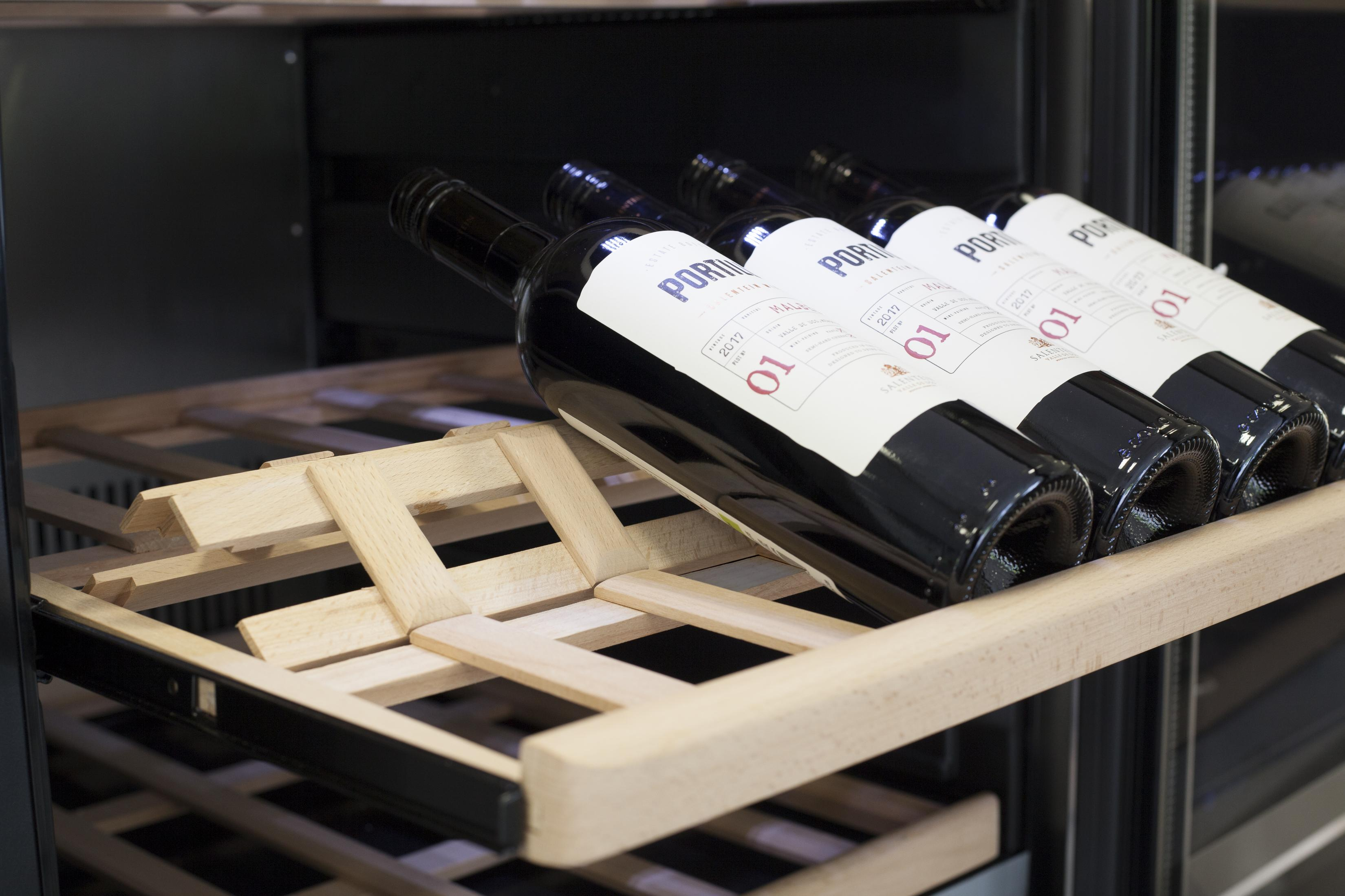 Flaschen mit rotem Wein auf einem Holzlagerregal in einem Weinkühlschrank.