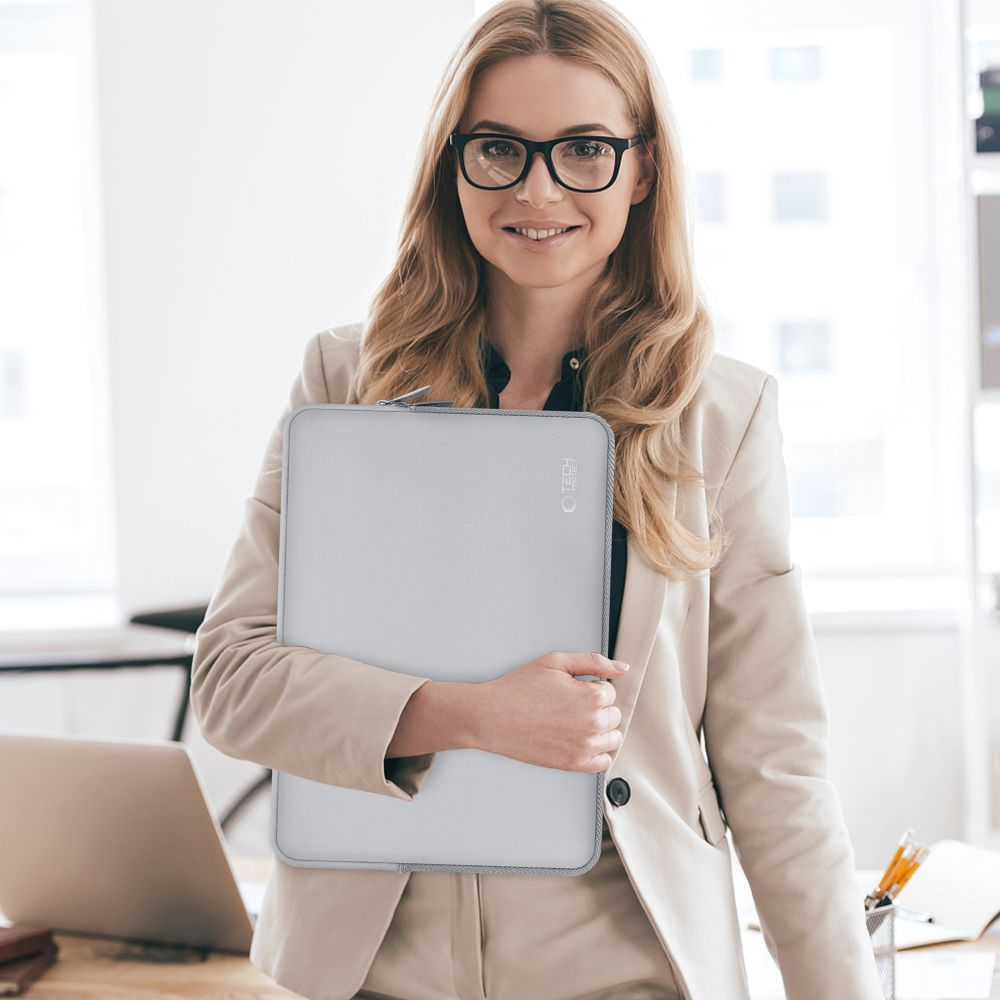 Eine Frau mit Brille hält eine graue Laptoptasche im Büro.
