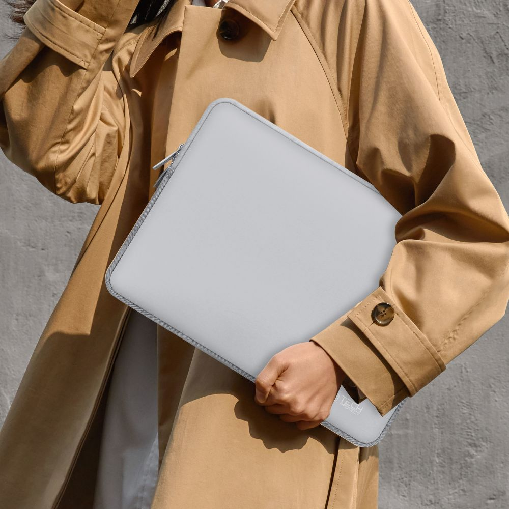 Eine Person in einem beigen Mantel hält eine graue Laptoptasche mit Reißverschluss.
