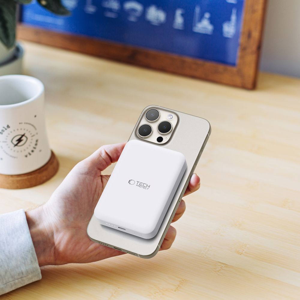 Eine weiße Powerbank lädt ein Handy, das auf einem Holztisch liegt.