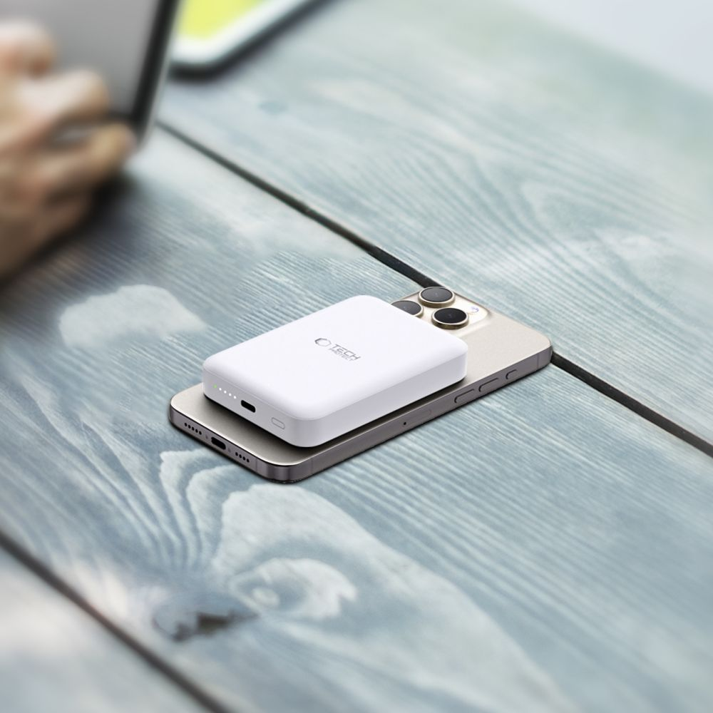 Weiße Powerbank auf einem goldenen iPhone auf einem blauen Holztisch. Eine Hand ist im Hintergrund unscharf.