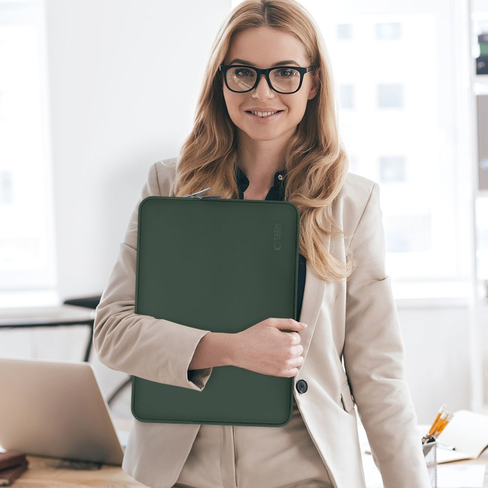 Eine Frau mit Brille hält eine grüne Laptoptasche in einem Büro.