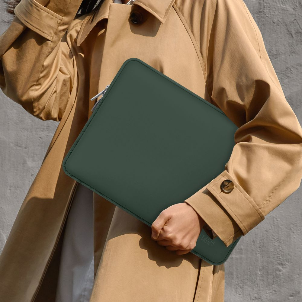 Eine Person in einem beigefarbenen Trenchcoat hält eine dunkelgrüne Laptoptasche.