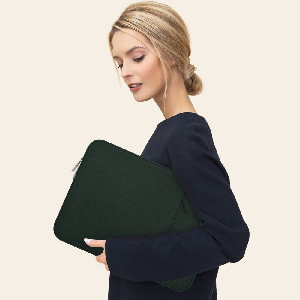 Eine Frau mit blondem Haar in einem dunklen Oberteil hält eine grüne Laptoptasche.