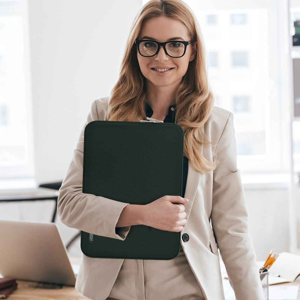 Eine Frau mit Brille hält eine dunkle Laptoptasche. Sie trägt einen beigefarbenen Anzug.