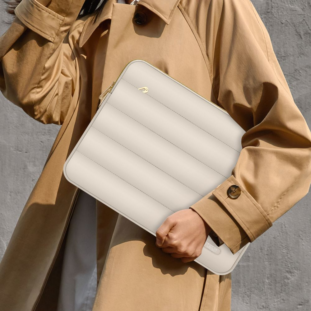 Eine Person im beigen Trenchcoat hält eine gesteppte weiße Laptoptasche.